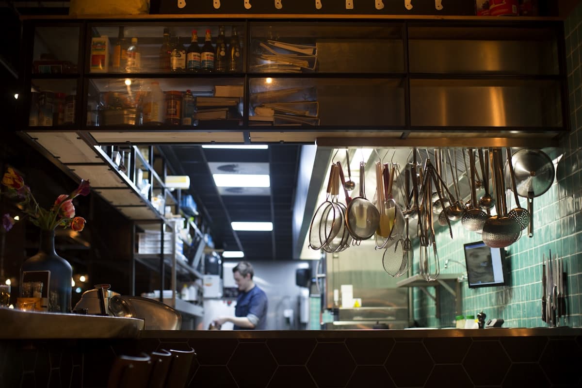 A cook working the line seen through the pass, copper pans hanging above the counter